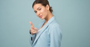 A young woman in a blue suit exhibits confidence with a relaxed pose against a blue background.